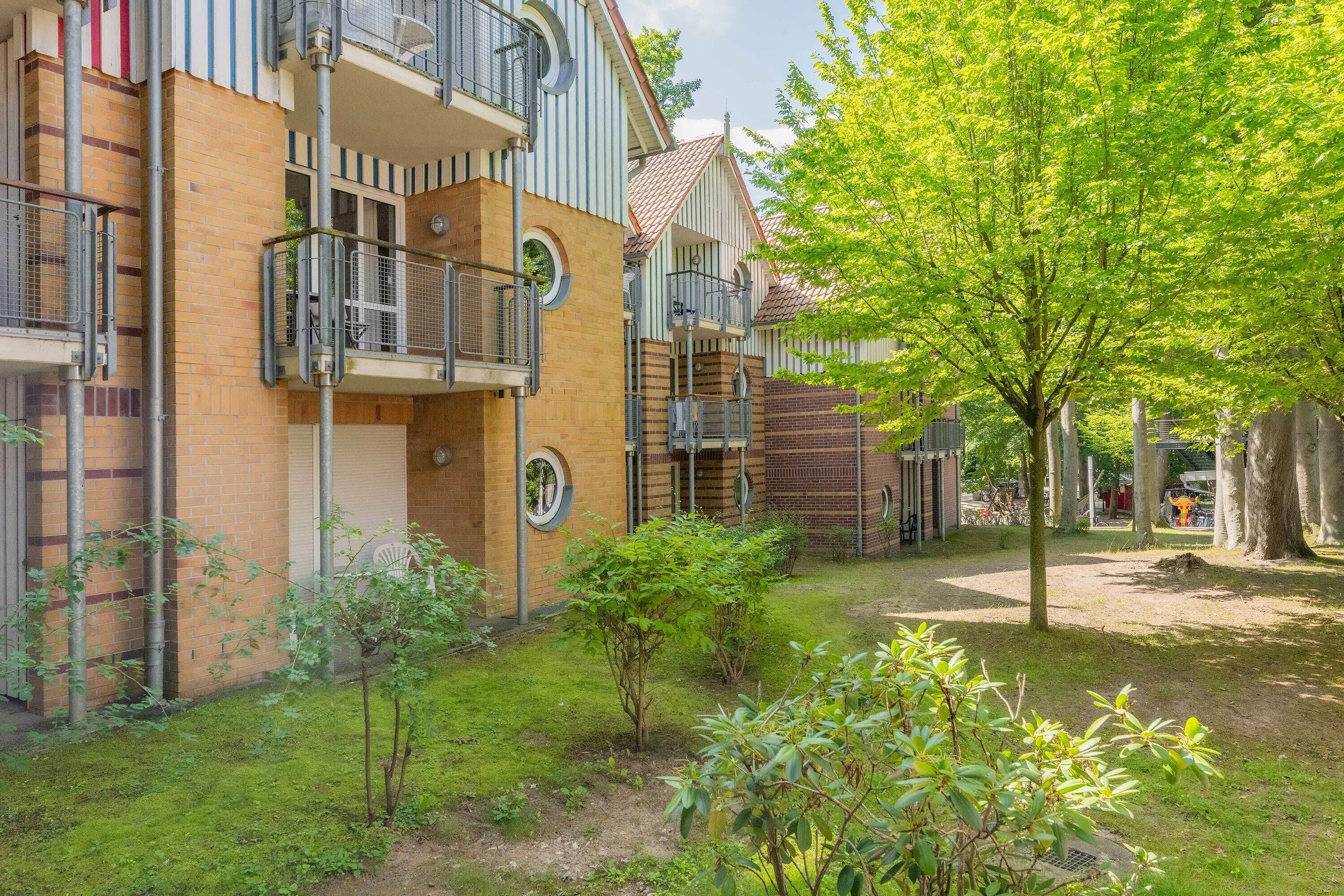 Un edificio residencial con varios balcones, fachada de ladrillo y un pequeño jardín con árboles y arbustos.