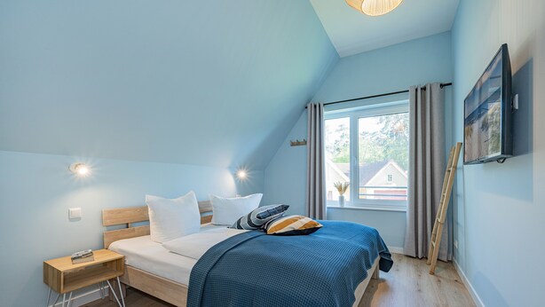 A bedroom with a bed, a nightstand, a window with curtains, and a painting on the wall.