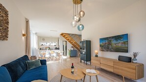 A modern living room with a blue sofa, a wooden dining table, and a kitchen in the background.