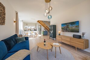 A modern living room with a blue sofa, a wooden dining table, and a kitchen in the background.