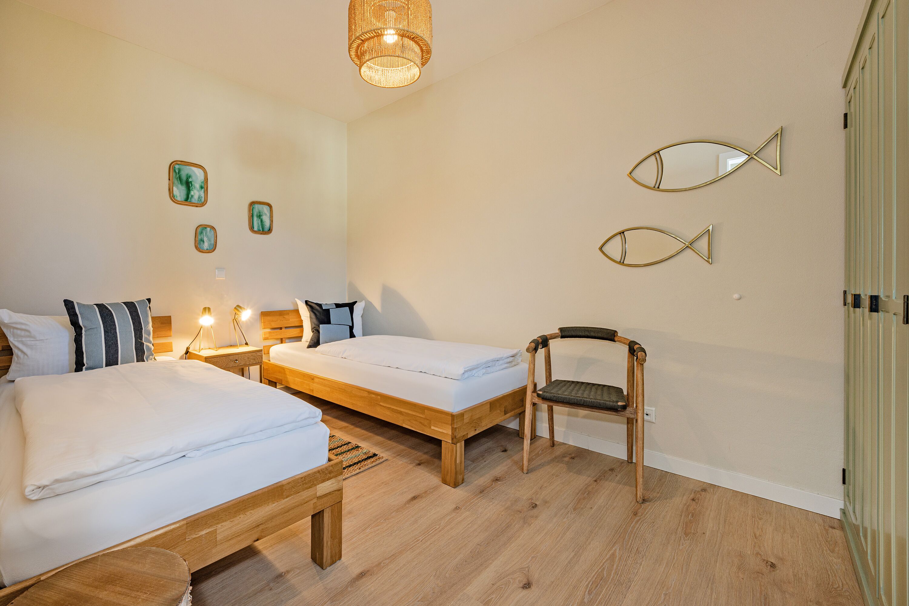 A hotel room with two beds, a wooden chair, and wall-mounted fish-shaped mirrors.