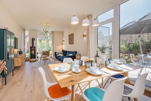 A modern dining area with a wooden table set for four, surrounded by white chairs with colorful cushions.