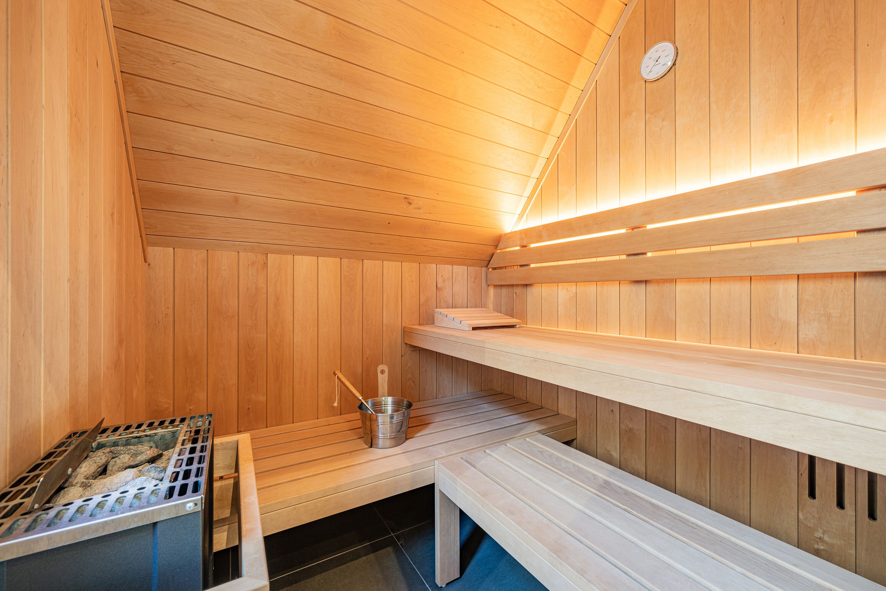 A sauna with wooden walls and benches, a metal bucket, and a stove.