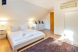 Een moderne slaapkamer met een groot bed, nachtkastjes, een dressoir en een kleurrijk vloerkleed.