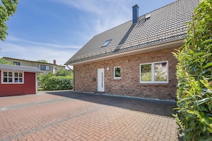 A brick house with a tiled roof, a small attached garage, and a paved driveway.