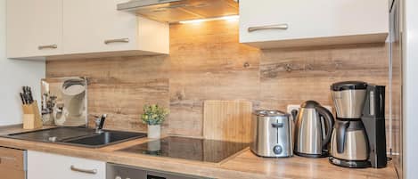 A modern kitchen with a built-in oven, a coffee maker, a toaster, and a kettle.