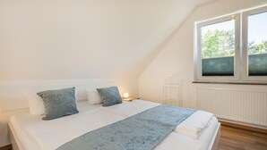 A bedroom with a bed, pillows, a bedside table with a lamp, and a window with blinds.