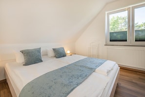 A bedroom with a bed, pillows, a bedside table with a lamp, and a window with blinds.