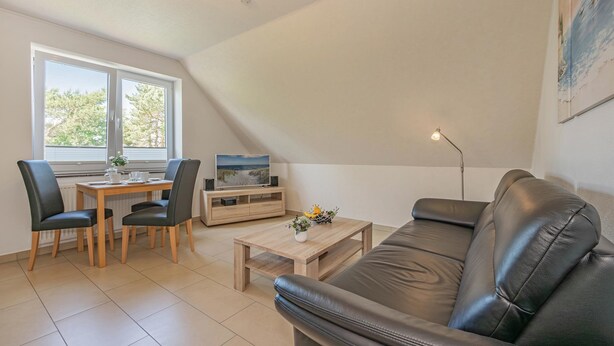 A modern living room with a sofa, a dining table with chairs, a coffee table, and a TV on a wooden stand.