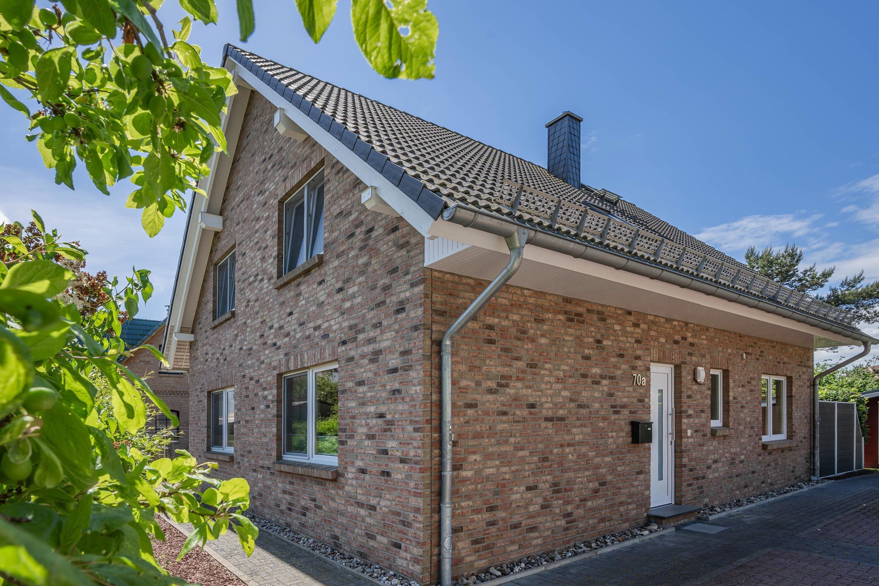 Une maison à deux étages, construite en briques, avec un toit en pente, une cheminée et une porte blanche.