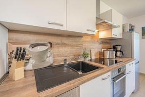 A modern kitchen with a black sink, stainless steel appliances, and wooden cabinetry.