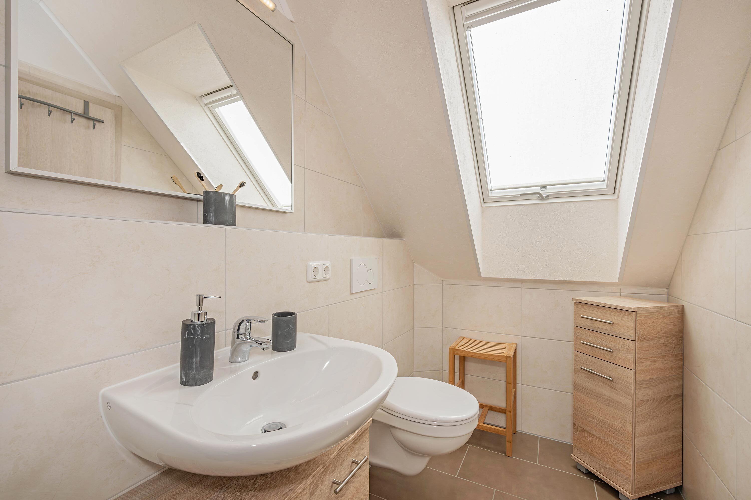 A modern bathroom with a skylight, a large sink, a toilet, and a wooden cabinet.