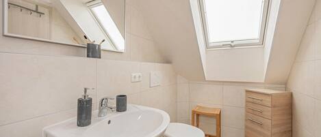 A modern bathroom with a skylight, a large sink, a toilet, and a wooden cabinet.