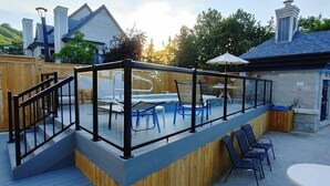 A deck with a glass railing, outdoor furniture, and a view of a house in the background.