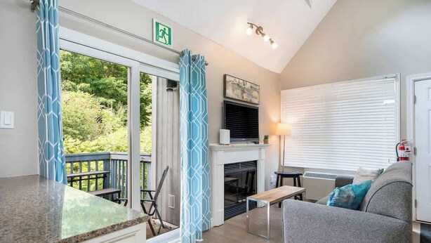A cozy living room with a fireplace, a sofa, a coffee table, and a view of the outdoors.