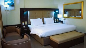 Ein Hotelzimmer mit einem großen Bett, einem Nachttisch mit Lampe, einem Sessel, einer Bank und einem wandmontierten Spiegel.