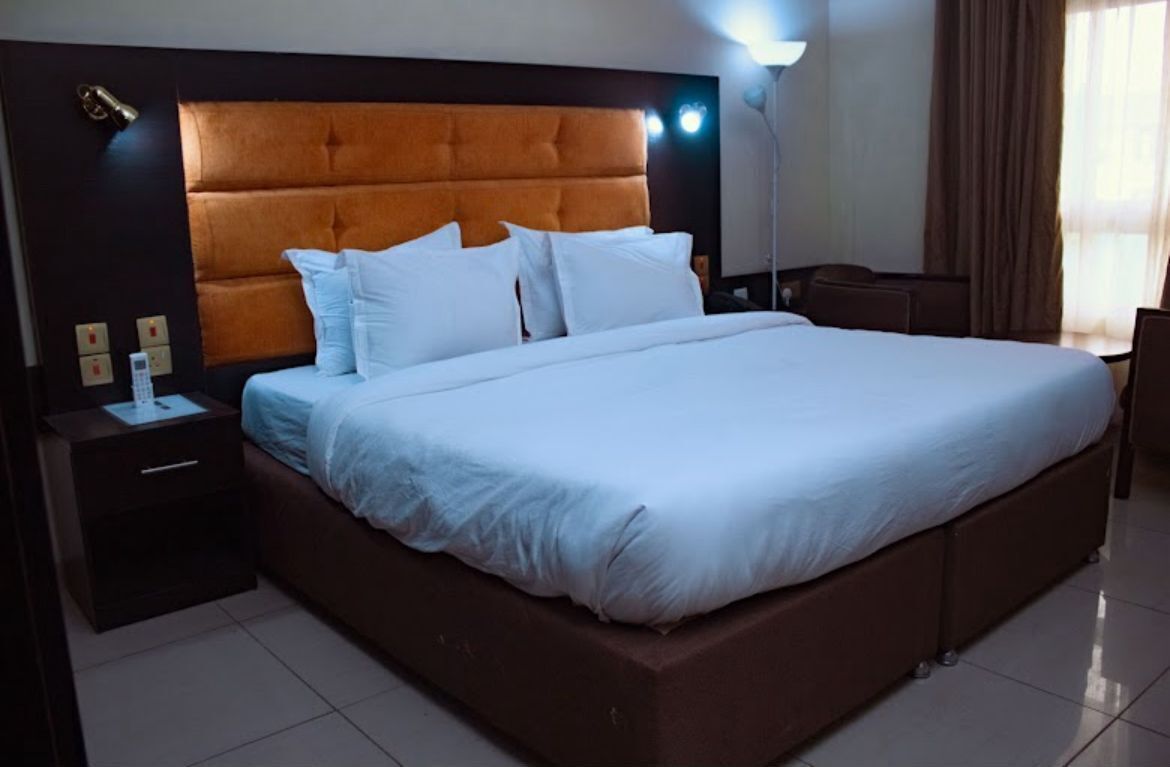 A hotel room with a large bed, a nightstand, a lamp, and a window with curtains.