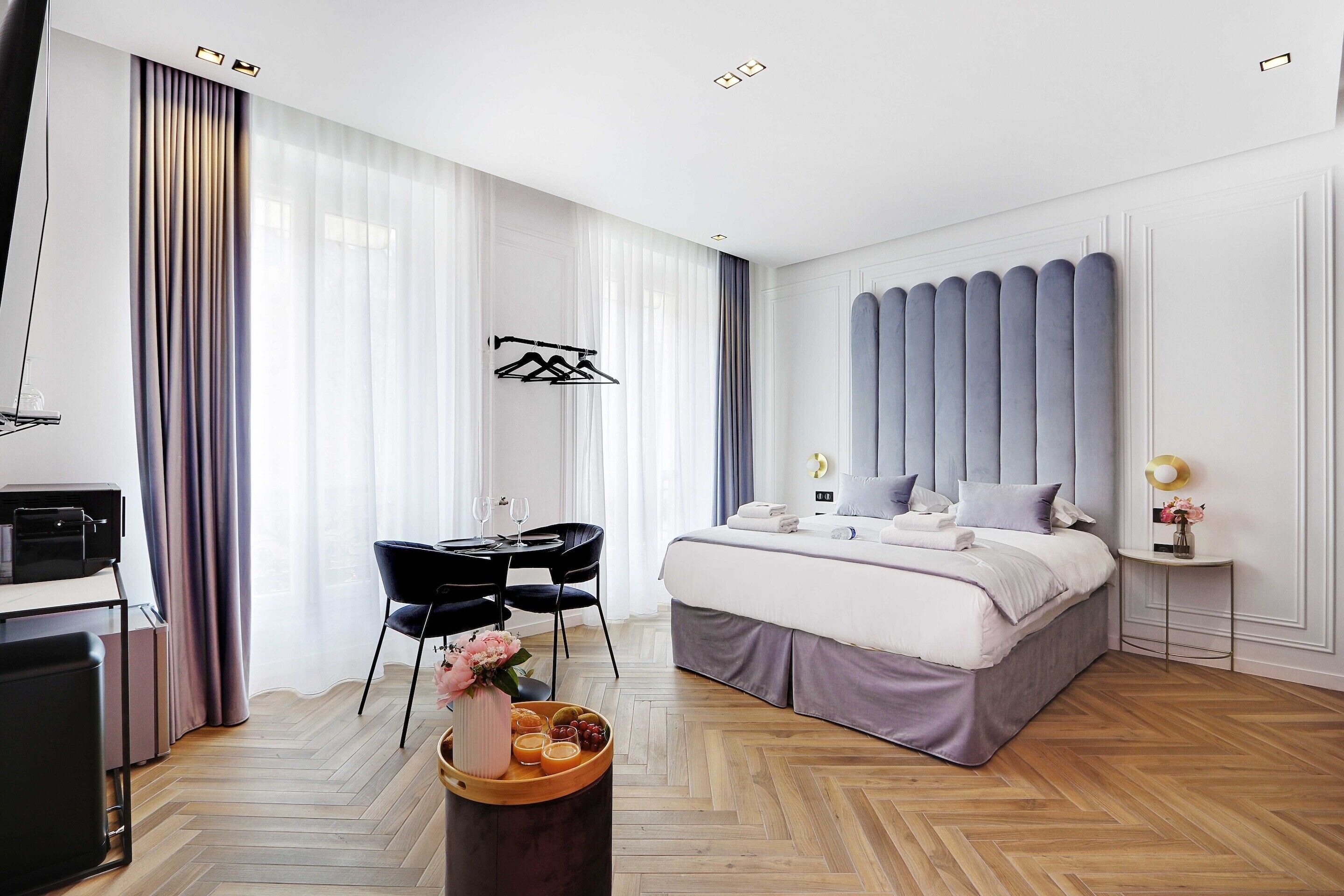 Une chambre d’hôtel moderne avec un grand lit, un bureau avec une chaise, une télévision et une petite table agrémentée d’un vase et de fruits.