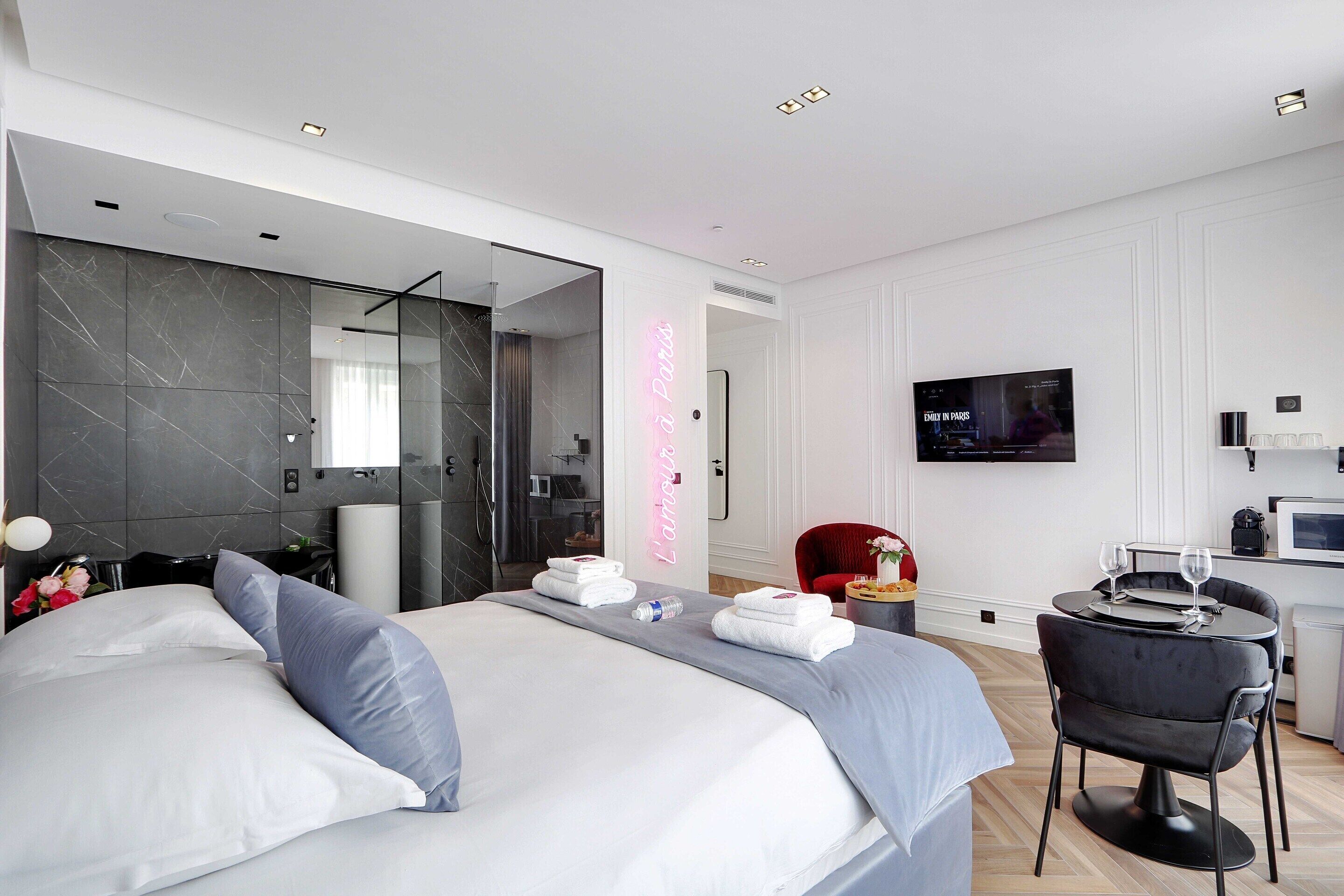 A modern hotel room with a large bed, a small desk with a chair, a TV, and a shower area.