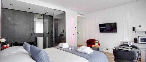 Una habitación de hotel moderna con una cama grande, un escritorio pequeño con una silla, un televisor y zona de ducha.