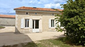 A two-story stone building with a tiled roof, white shutters, and a small porch area. - Renovated Charentais house in peaceful setting with parking and private garden (Challignac)