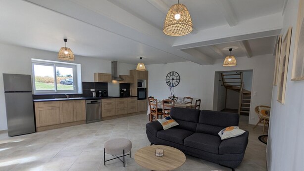 A modern kitchen with wooden cabinets, a stainless steel refrigerator, and a dining area with a sofa and table. - Renovated Charentais house in peaceful setting with parking and private garden (Challignac)