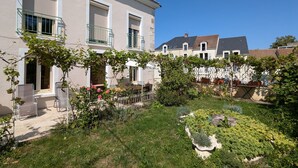 En bostadsbyggnad med en trädgårdsyta som har en pergola med klätterväxter och ett urval av buskar.