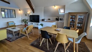 En rymlig lägenhet i loftstil med matplats, kök och en stor TV.