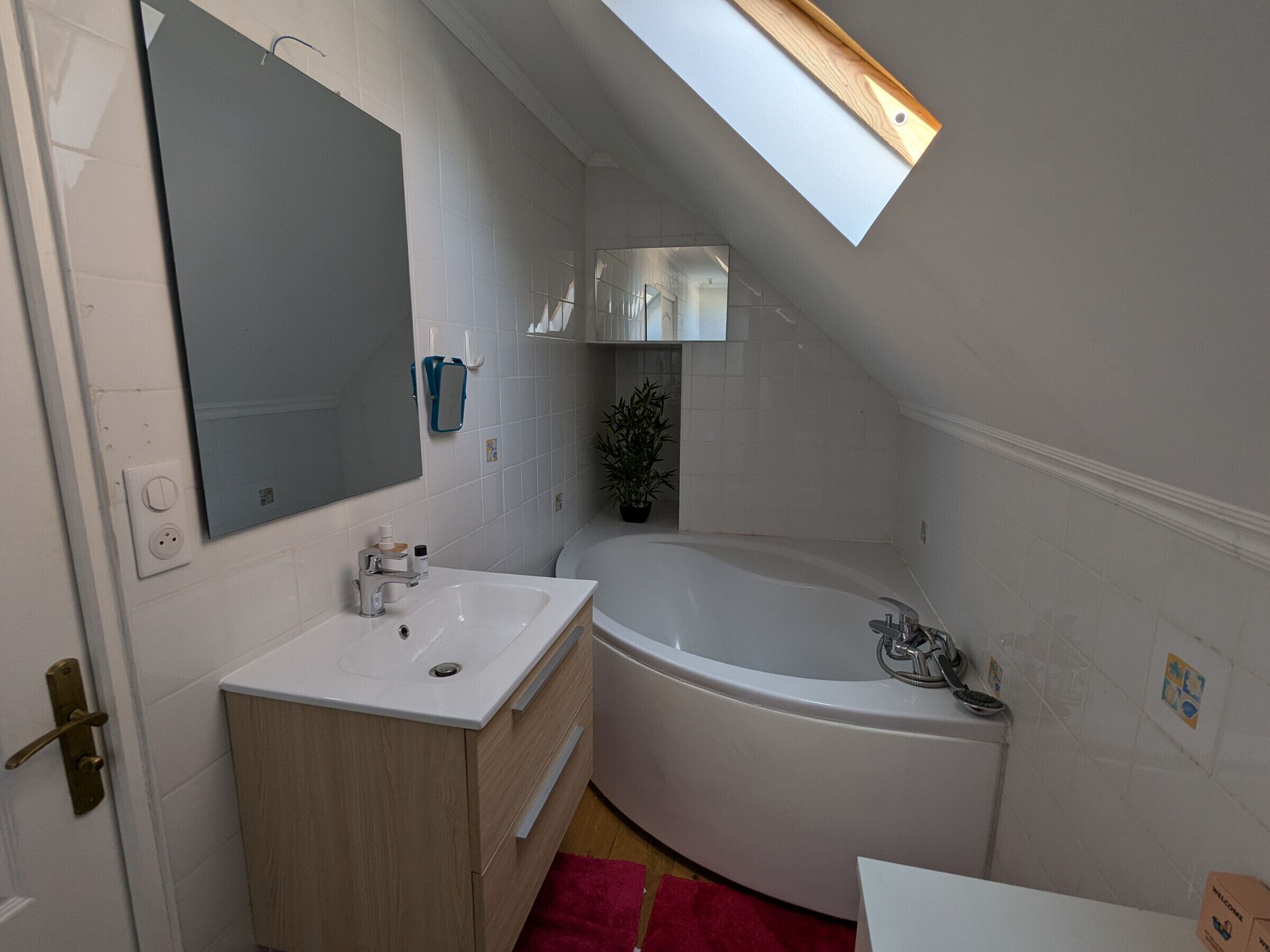 Ein modernes Badezimmer mit einer freistehenden Badewanne, einem großen Spiegel und einem Dachfenster.