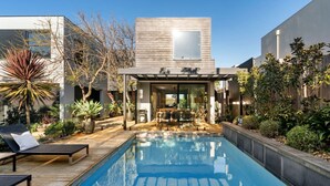 A modern outdoor pool area with a wooden deck, lounge chairs, and a pergola. - Villa Sorrento | The Perfect Escape (Sorrento)