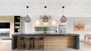 A modern kitchen with a large island, bar stools, pendant lights, and a built-in bookshelf. - Villa Sorrento | The Perfect Escape (Sorrento)