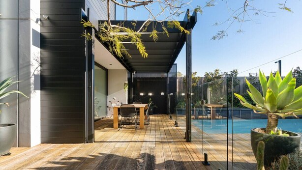 A modern outdoor deck with a wooden floor, a dining table, chairs, and a glass enclosure for a pool. - Villa Sorrento | The Perfect Escape (Sorrento)