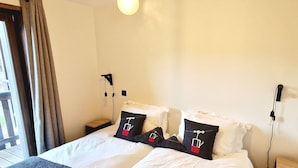 A double bed with white and dark grey bedding, two pillows with a tag design, a bedside table, and a nightstand with a lamp.