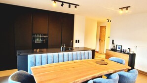 A modern kitchen with dark cabinets, a central island, and a dining area with a wooden table and blue upholstered chairs.