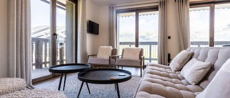 Una sala de estar moderna con un sofá, dos mesas auxiliares, un sillón y un televisor montado en la pared.