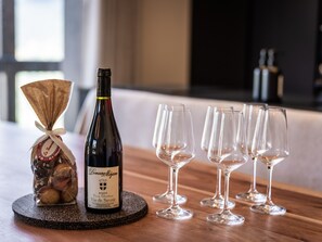 Uma garrafa de vinho Domaine de la Pierre sobre um apoio, com uma pequena sacola de presente ao lado, e vários copos de vinho em uma superfície de madeira.