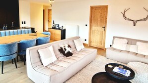 A modern living room with a sofa, a coffee table, and a dining area with blue chairs.