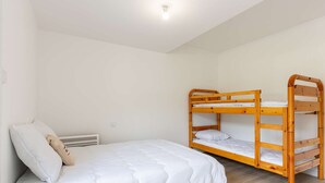 Ein Einzelbett mit weißer Bettdecke und Kissen, ein Holzhochbett zur Rechten und eine weiße Decke mit einer Leuchte.