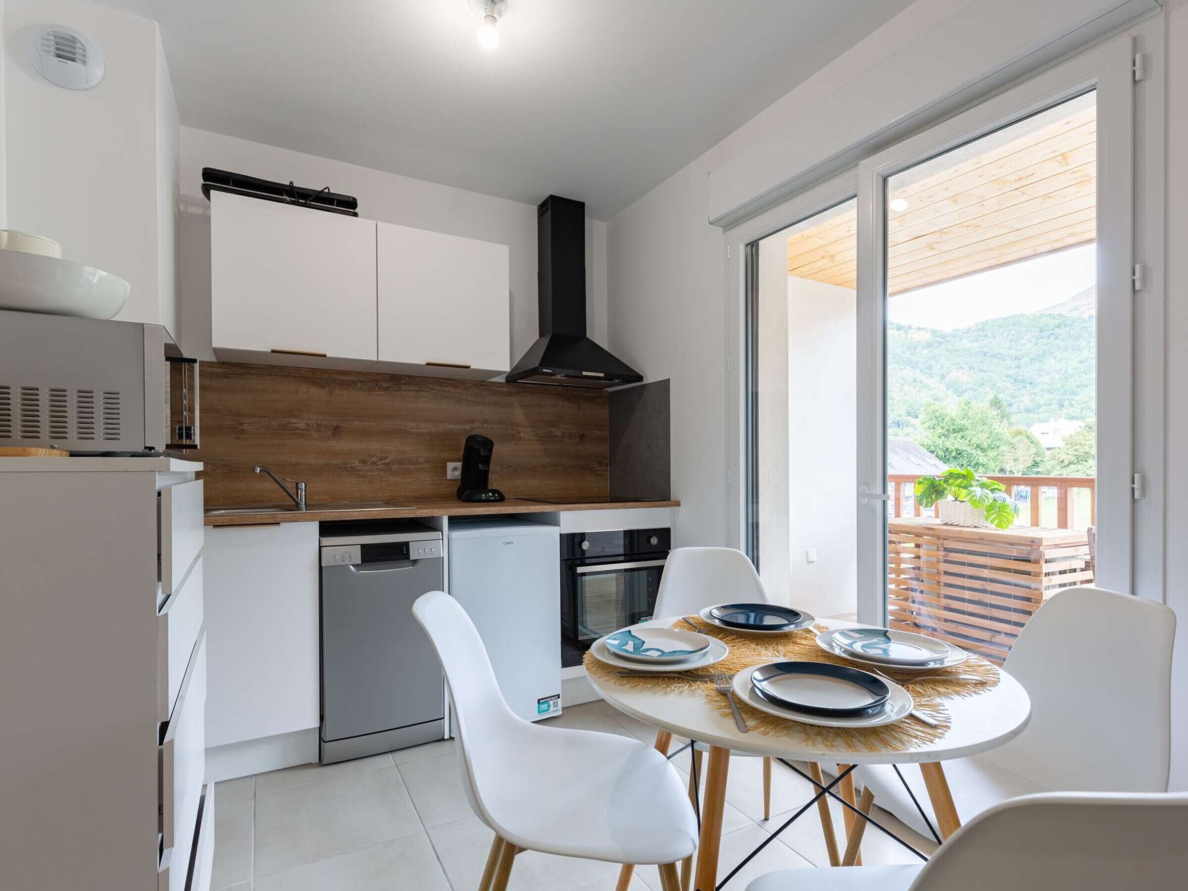Una cocina moderna con armarios blancos, una campana extractora negra y un comedor con una mesa redonda para cuatro.