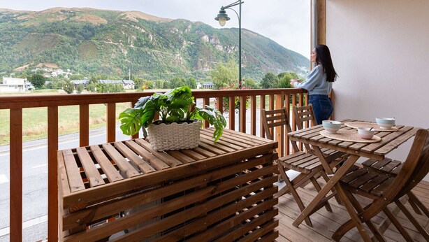 Eine Holzterrasse mit Tisch und Stühlen, einem Blumentopf und Blick auf einen Berg.