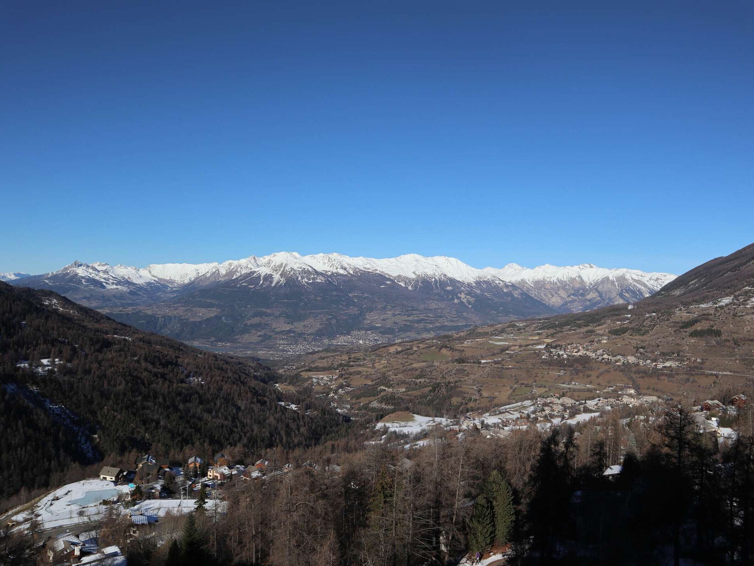 Paisaje montañoso con picos nevados y un valle con edificios dispersos.