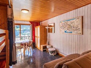 A cozy room with a wooden ceiling, a dining area with a table and chairs, a sofa, a cabinet, and a map on the wall.