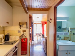 A narrow kitchen with a stove, sink, and a red apron hanging on the wall.