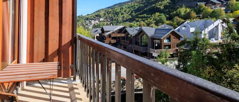 A balcony with wooden railings overlooking a village with traditional wooden buildings and a mountainous backdrop.