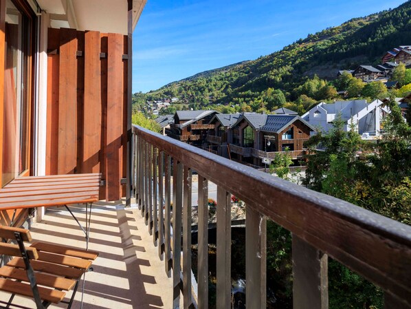 A balcony with wooden railings overlooking a village with traditional wooden buildings and a mountainous backdrop.