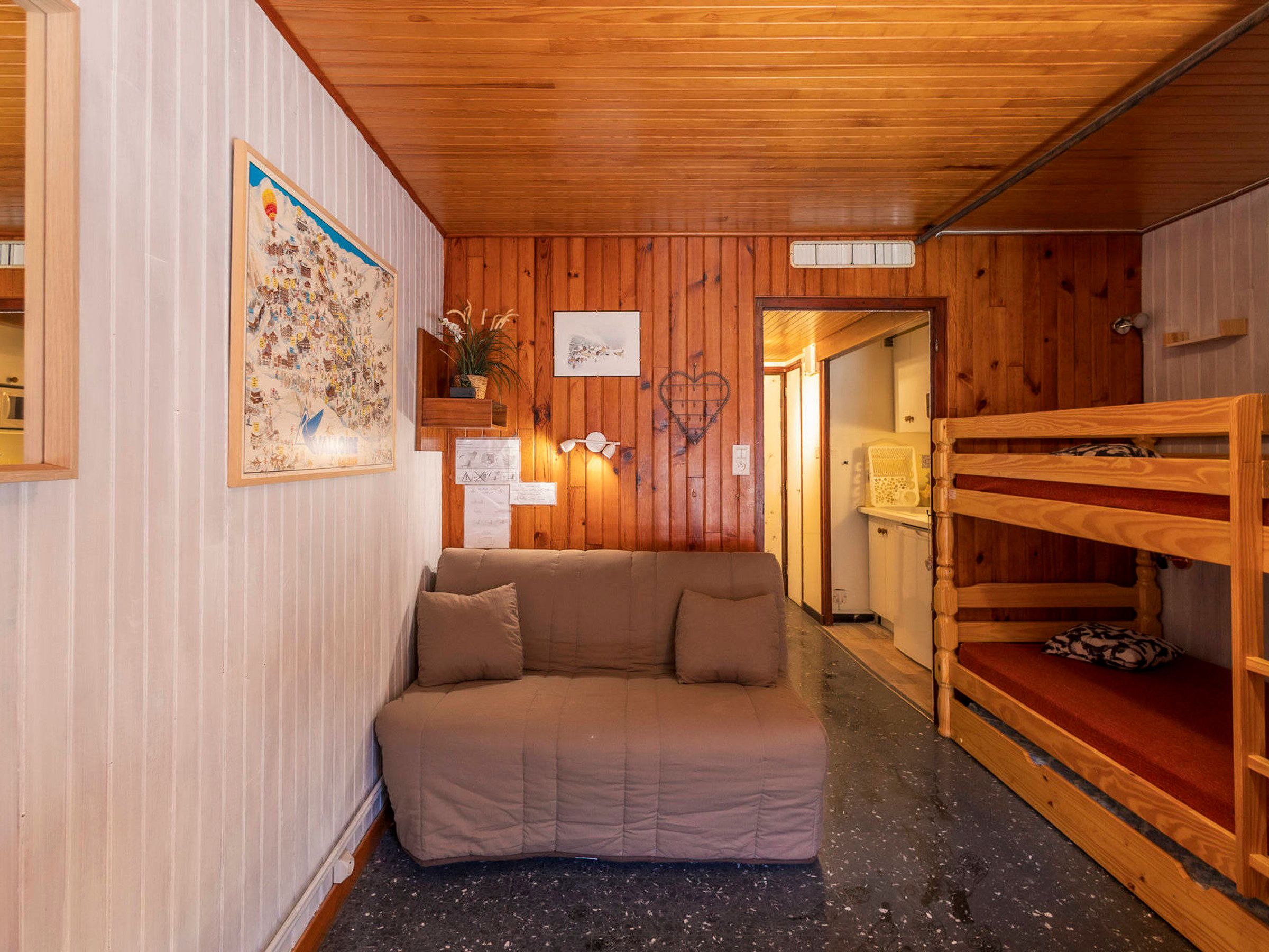 A cozy room with a wooden ceiling, a sofa, a wooden bench, and a wall with a framed picture and some papers.