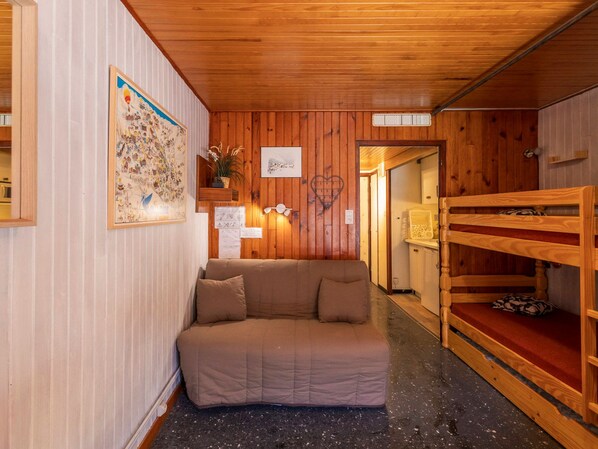 A cozy room with a wooden ceiling, a sofa, a wooden bench, and a wall with a framed picture and some papers.