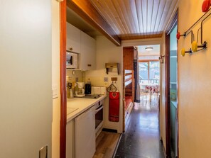 A narrow kitchen with a microwave, toaster, and coffee maker. A red towel hangs on the oven door.