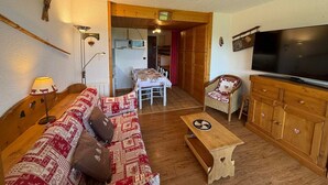 Una sala de estar acogedora con un sofá de madera, un televisor, un mueble de madera y una zona de comedor al fondo.