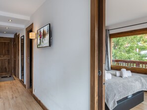 Een slaapkamer met een bed, een raam met uitzicht op bomen en een deur naar een andere kamer.